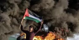 شاب فلسطيني يرفع علم فلسطين خلال مواجهات مع الاحتلال.