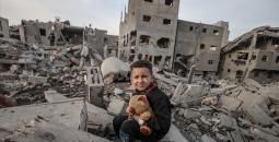 طفل فلسطيني يحمل دميته فوق منزل عائلته المدمر في قطاع غزة.jpg