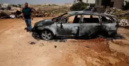 فلسطيني يقف بجانب مركبة أحرقها المستوطنون.webp