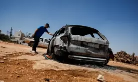 فلسطيني يتفقد سيارة محترقة بعد هجوم شنه مستوطنون على قرية كفر مالك.webp
