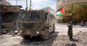 مسن يرفع علم فلسطين قرب آلية عسكرية إسرائيلية.jpg