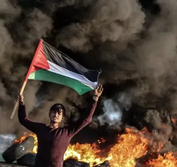 شاب فلسطيني يرفع علم فلسطين خلال مواجهات مع الاحتلال