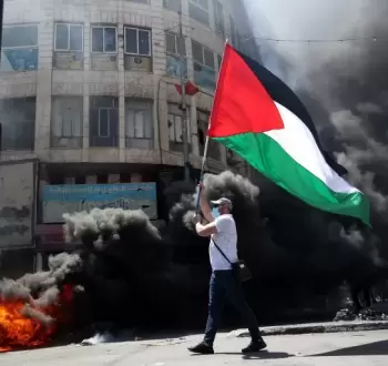 شاب فلسطيني يرفع علم فلسطين خلال مواجهات بالضفة