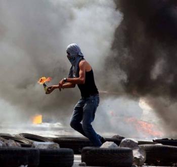 شاب فلسطيني يُلقي عبوة حارقة خلال مواجهات في الضفة الغربية.jpeg