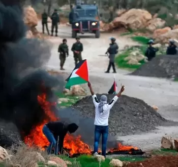 شاب فلسطيني يرفع علم فلسطين خلال مواجهات مع قوات الاحتلال بالضفة الغربية