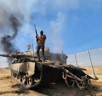 مقاوم فلسطيني يرفع بندقيته فوق دبابة ميركافاة إسرائيلية بعد تدميرها في غلاف غزة.jpeg