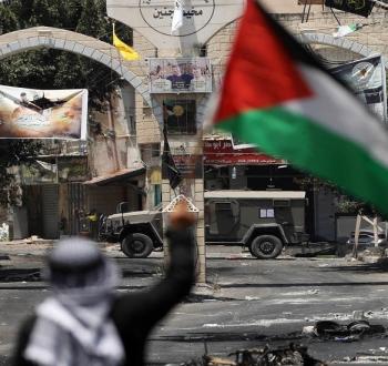 مواطن فلسطيني يرفع علم فلسطين أمام مخيم جنين.jpg