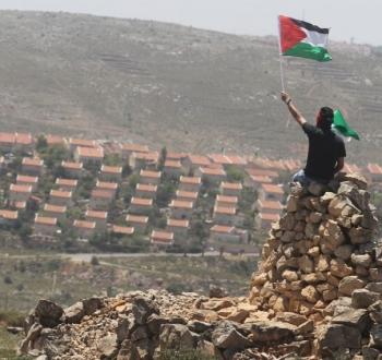 فلسطيني يرفع علم فلسطين مقابل مستوطنة في رام الله.jpg
