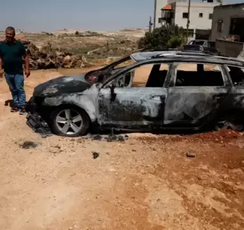 فلسطيني يقف بجانب مركبة أحرقها المستوطنون.webp