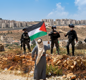 فلسطيني يرفع علم فلسطين في وجه قوات الاحتلال متحديا توغل الاستيطان بالضفة