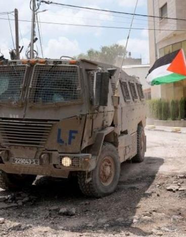 مسن يرفع علم فلسطين قرب آلية عسكرية إسرائيلية.jpg