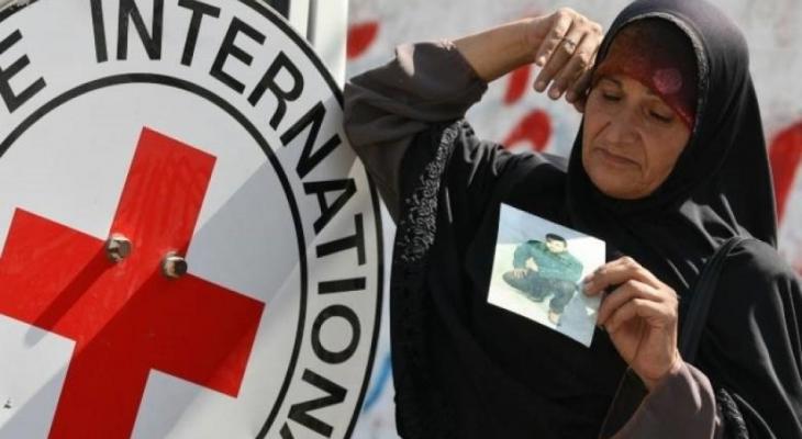 سيدة فلسطينية تحمل صورة نجلها الأسير بجانب شعار الصليب الأحمر.jpg