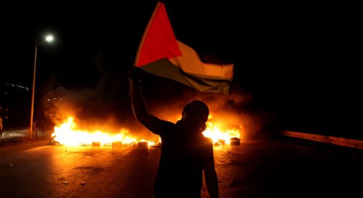 شاب فلسطيني يرفع علم فلسطين خلال مواجهات ليلية في الضفة الغربية.jpg
