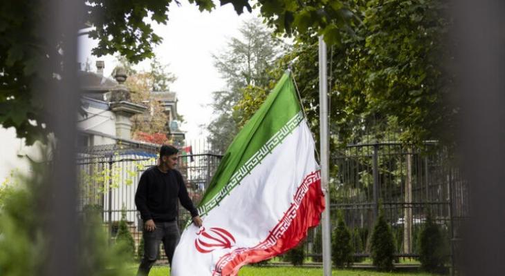 مواطن إيراني يقف قرب علم الجمهورية الإيرانية الإسلامية.jpg