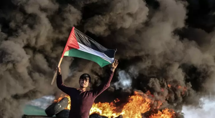 شاب فلسطيني يرفع علم فلسطين خلال مواجهات مع الاحتلال