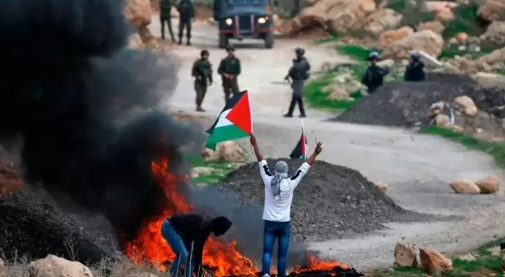 شاب فلسطيني يرفع علم فلسطين خلال مواجهات مع قوات الاحتلال بالضفة الغربية.webp