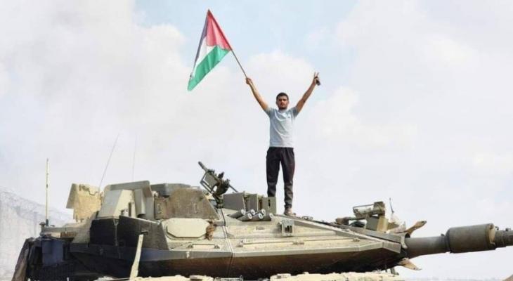 شاب فلسطيني من غزة يرفع علم فلسطين وشارة النصر فوق الميركافاة الإسرائيلية.jpg