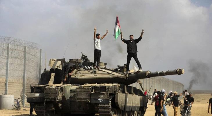 فلسطينيون يرفعون علم فلسطين وشارة النصر فوق الميركافاة الإسرائيلية.jpeg