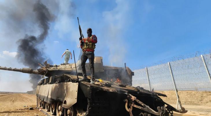 مقاوم فلسطيني يرفع بندقيته فوق دبابة ميركافاة إسرائيلية بعد تدميرها في غلاف غزة.jpeg