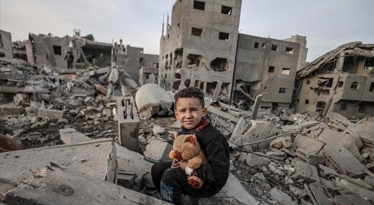 طفل فلسطيني يحمل دميته فوق منزل عائلته المدمر في قطاع غزة.jpg
