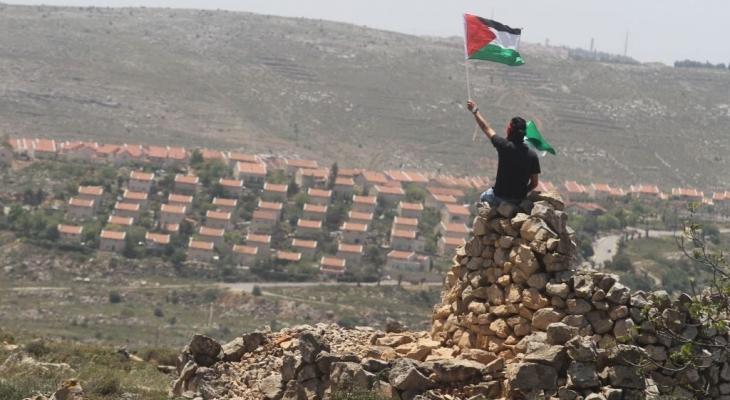 فلسطيني يرفع علم فلسطين مقابل مستوطنة في رام الله.jpg