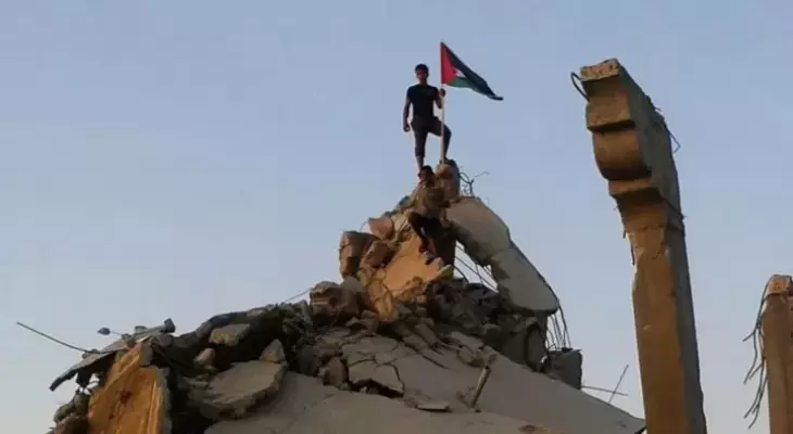 شاب يرفع علم فلسطين على منزل مدمر في غزة.webp