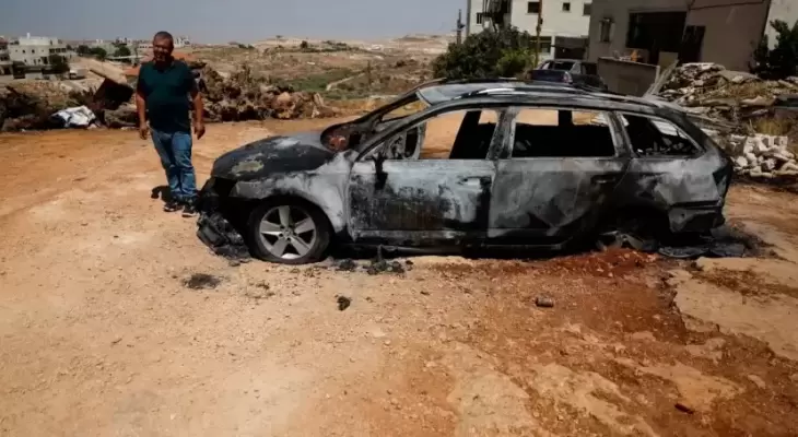فلسطيني يقف بجانب مركبة أحرقها المستوطنون.webp
