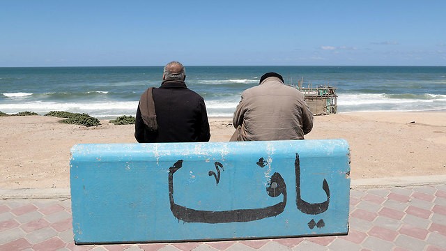 يجلس الصياد محمود العاصي على مقعد خرساني على شاطئ غزة مع التعليق يافا وفقا له ، نشأ في يافا وطرد منها في عام 1948.jpg